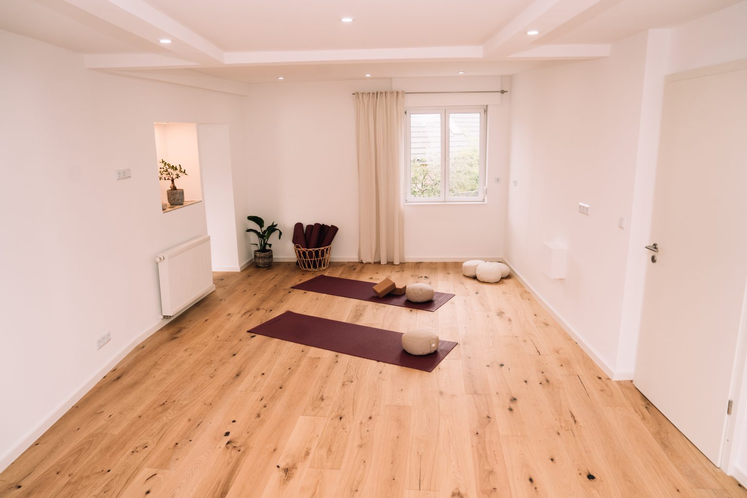 Heller Kursraum mit Holzboden, Fenster und zwei Yogamatten