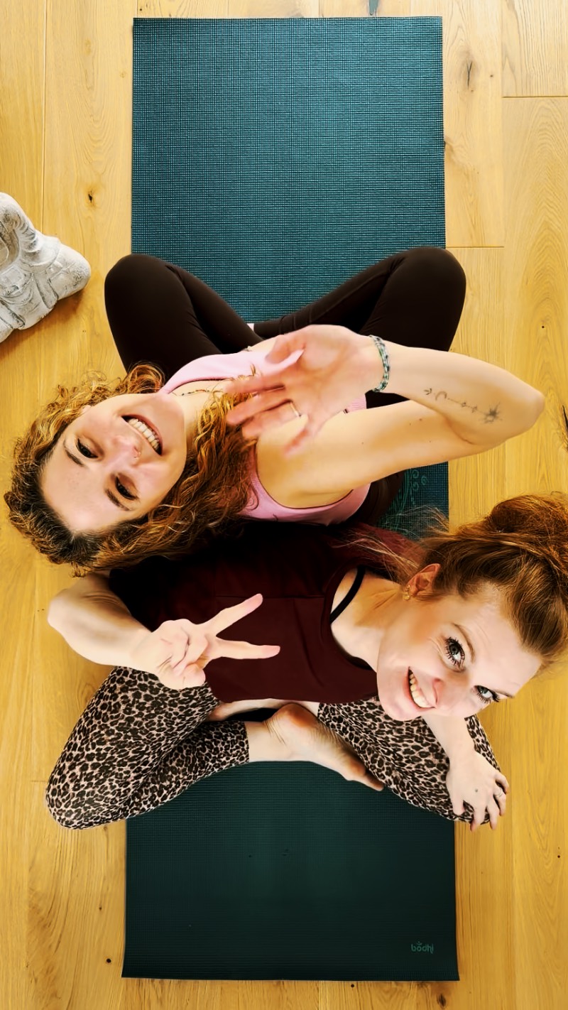 Charlena und Franzi liegen lachend auf einer Yogamatte